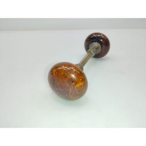 May include: An antique door knob with a brown, marbled finish. The knob has an oval shape and is connected to a smaller, round knob by a brass rod. The knobs are a dark brown color with a swirled pattern.