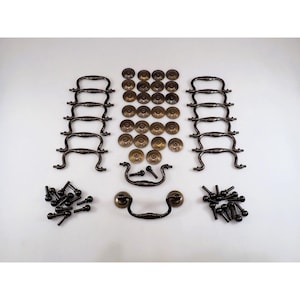 May include: A collection of antique brass furniture hardware including twelve curved bail pulls, twenty-four circular backplates, and twenty-four matching mounting screws arranged in organized rows on a plain surface for furniture restoration.