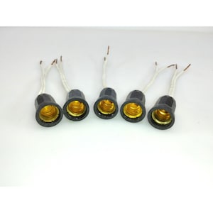 May include: Five black light bulb sockets with gold-colored interiors and white wires extending from the top. The sockets are arranged in a row against a white background. The wires have exposed copper ends.