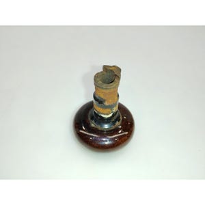 May include: A vintage bottle stopper with a dark brown, rounded base and a cylindrical neck. The neck is composed of a rusty metal top, a black band, and a brown section. The stopper is designed to fit into a bottle.