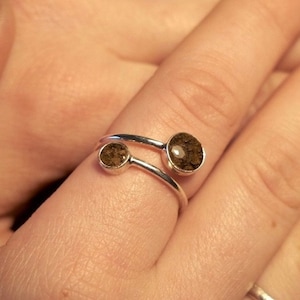 May include: A silver ring with two brown stones set in the band. The ring is worn on a finger.