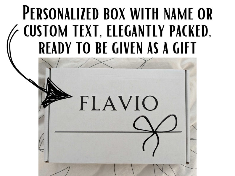 May include: A white gift box with a black ribbon and bow. The box is personalised with the name "FLAVIO" printed in black.