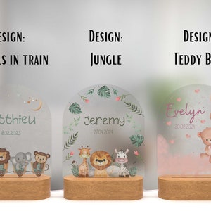 May include: Three personalised night lights with different designs. The first features a train with animals, the second has a jungle theme, and the third has a teddy bear with balloons. Each light has a wooden base and a frosted glass panel with a name and date.