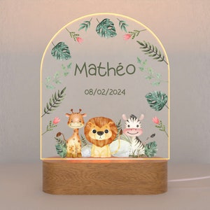 May include: A wooden night light with a clear acrylic insert featuring a jungle theme. The insert has a giraffe, lion, and zebra with green leaves and pink flowers. The text "Math&eacute;o 08/02/2024" is printed on the insert.