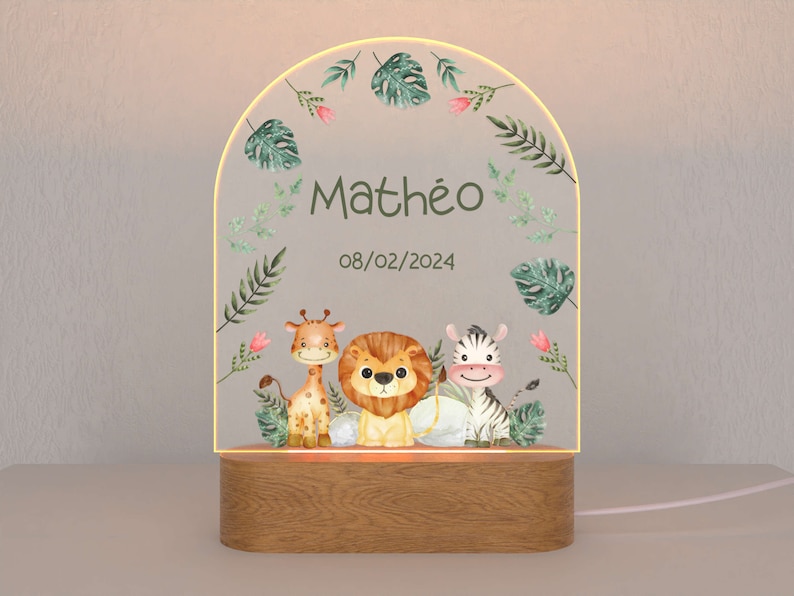 May include: A wooden night light with a clear acrylic insert featuring a jungle theme. The insert has a giraffe, lion, and zebra with green leaves and pink flowers. The text "Math&eacute;o 08/02/2024" is printed on the insert.