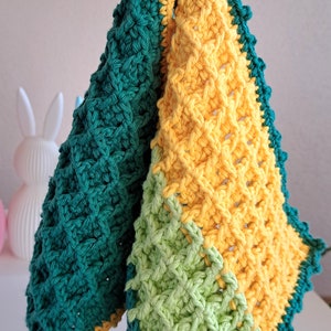 Könnte beinhalten: Zwei gehäkelte Geschirrtücher in Grün, Gelb und Hellgrün. Die Geschirrtücher haben einen gewellten Rand und sind mit einem strukturierten Stich gearbeitet.