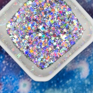 May include: A white square container filled with iridescent glitter. The glitter is a mix of silver, blue, pink, and green.
