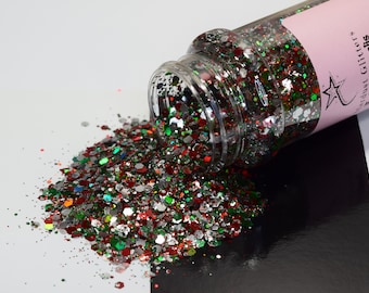 May include: A clear jar filled with red, green, silver, and white glitter. The jar is tipped over, spilling the glitter onto a white surface. The label on the jar reads "Star Dust Glitter - Chunky/Cdx - Polaris Borealis".
