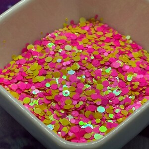 May include: A white bowl filled with pink and yellow glitter. The glitter is in the shape of small circles.