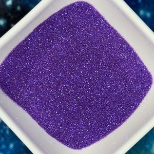 May include: A small white square dish filled with purple glitter.