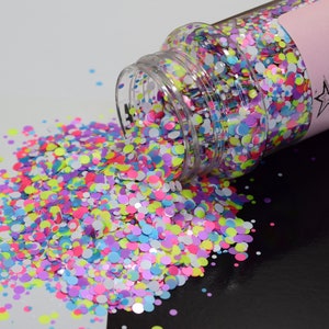 May include: A clear jar filled with colorful confetti glitter. The glitter is a mix of pink, blue, green, yellow, and white. The jar is tipped over and the glitter is spilling out onto a white surface.