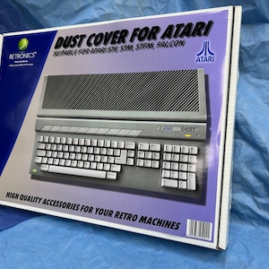 Puede incluir: Una caja blanca con una imagen de una computadora Atari 1040ST gris. La caja dice "Dust Cover for Atari" y "Suitable for Atari STE, STM, STFM, Falcon". La caja también tiene el logotipo de Atari y el texto "High Quality Accessories for Your Retro Machines".
