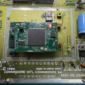 Op de afbeelding: Close-up van een Commodore 64 printplaat. De groene printplaat bevat diverse elektronische componenten, waaronder chips, condensatoren en weerstanden. De tekst "COMMODORE INTL COMMODORE 64" is zichtbaar, samen met "MADE IN HONG KONG" en het jaar 1986.