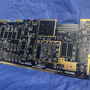 Peut inclure: Une carte de circuit imprimé noire Commodore 64 avec des accents dorés. La carte comporte de nombreux composants électroniques, notamment des puces, des connecteurs et des pistes. Le texte sur la carte comprend "COMMODORE 64" et "ASSY NO 250407".