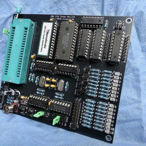 Könnte beinhalten: Eine schwarze Leiterplatte mit verschiedenen elektronischen Bauteilen, darunter Chips, Widerstände und Anschlüsse. Auf der linken Seite befindet sich eine grüne Buchse. Der Text "Z80 CPU Tester Rev.2.5" ist sichtbar. Dieser Artikel wird wahrscheinlich zum Testen oder Reparieren elektronischer Geräte verwendet.