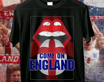 May include: Black t-shirt with a graphic featuring red lips, a white and red ball with a cross, and the text "COME ON ENGLAND" in blue. The design is set against a brick wall background.