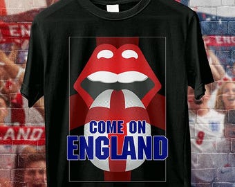 May include: Black t-shirt featuring a red and white design of a mouth and a soccer ball with the text "COME ON ENGLAND" in blue. The shirt is hanging on a wooden hanger.