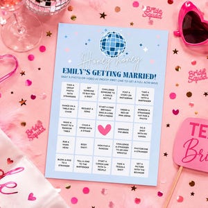 Pode incluir: Uma cena de despedida de solteira com um jogo, óculos de sol rosa e decorações. O cartão do jogo diz "Emily's Getting Married!" e inclui vários desafios. Uma faixa "Bride" e um letreiro "Team Bride" também são visíveis.