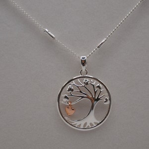 May include: Silver necklace with a tree of life pendant. The pendant is made of silver and features a tree with heart-shaped leaves. The heart at the bottom of the tree is rose gold.