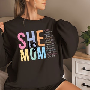 May include: Black sweatshirt with the text "SHE IS MOM" in rainbow colors. The text is surrounded by a list of words and bible verses describing the qualities of a mother.