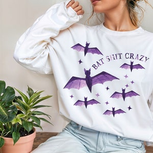 May include: White long-sleeved sweatshirt with a purple bat graphic and the text "Bat Shit Crazy".
