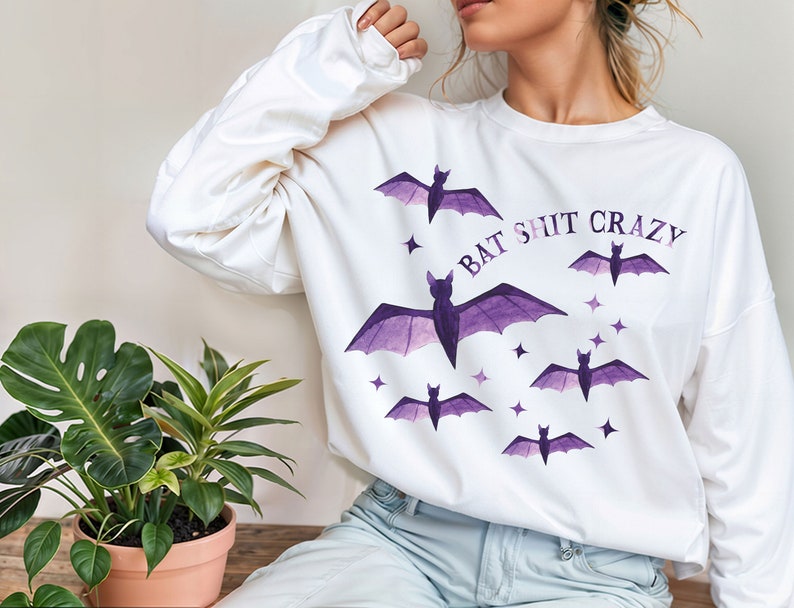 May include: White long-sleeved sweatshirt with a purple bat graphic and the text "Bat Shit Crazy".
