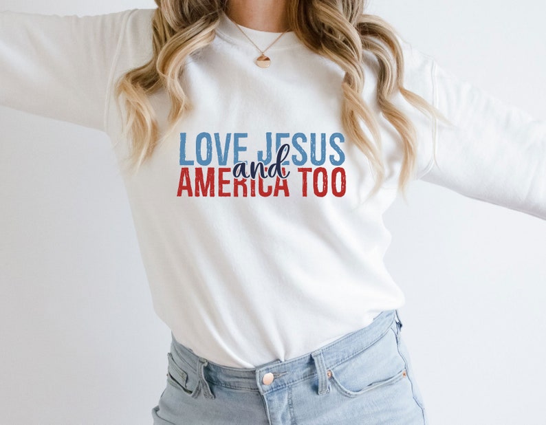 Op de afbeelding: Witte longsleeve sweatshirt met de tekst "LOVE JESUS and AMERICA TOO" in rode, blauwe en witte letters.