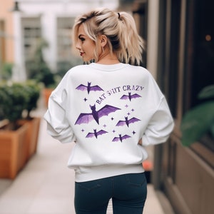May include: White sweatshirt with a purple bat design and the text "BAT SHIT CRAZY" on the back.