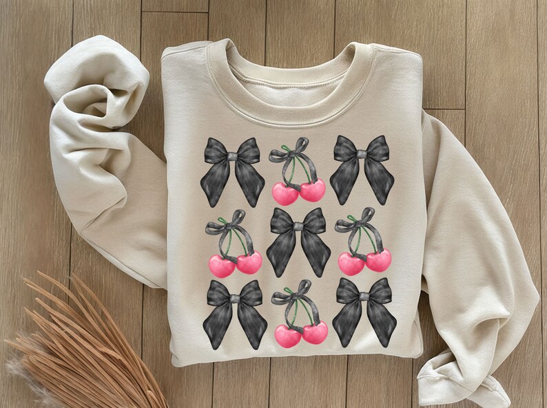 May include: A beige sweatshirt with a black and white cherry and bow pattern. The cherries are pink and the bows are black.