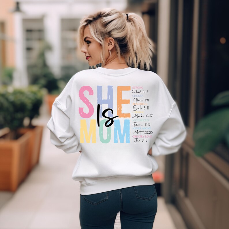 May include: White sweatshirt with the text "SHE IS MOM" in rainbow colors. The text is accompanied by bible verses describing the qualities of a mother.