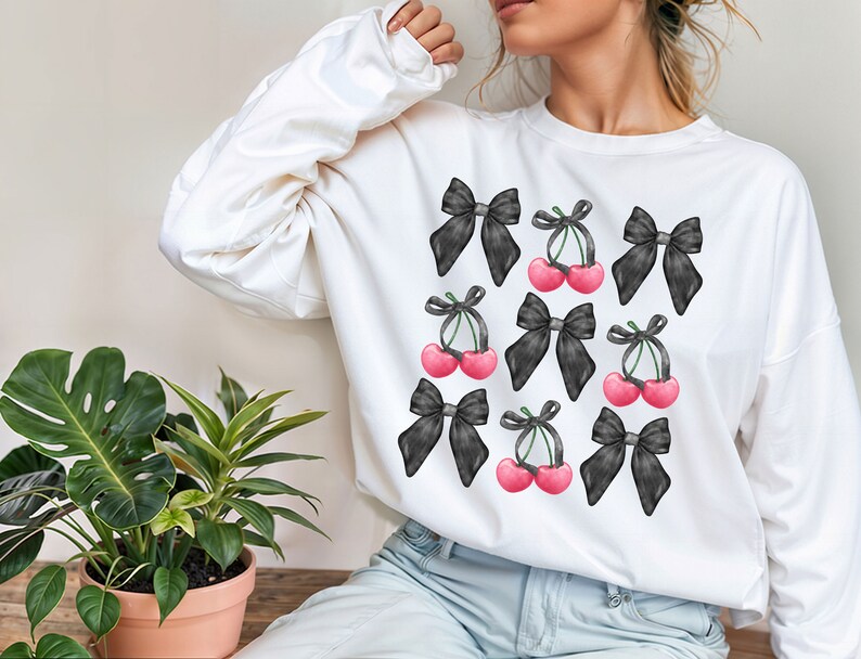 May include: White sweatshirt with a black and white print of cherries and bows. The cherries are pink and the bows are black.