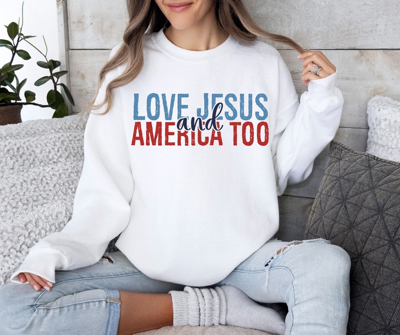 Op de afbeelding: Wit sweatshirt met de tekst "LOVE JESUS and AMERICA TOO" in rode, blauwe en witte letters.