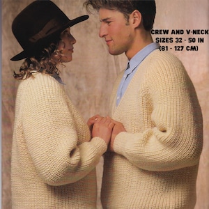 Op de afbeelding: Twee mensen dragen crèmekleurige Aran-gebreide truien. De trui aan de linkerkant heeft een ronde hals en de trui aan de rechterkant heeft een V-hals. De tekst op de afbeelding luidt "Fishermans Jumper Aran Yarn Crew and V-Neck Sizes 32-50 in (81-127 cm)"