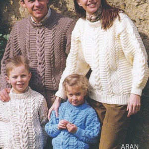 Puede incluir: Una familia de cuatro personas con suéteres de punto Aran. Los suéteres son de varios colores, incluyendo blanco, marrón y azul. Los suéteres presentan un patrón de punto de cable. El texto "ARAN 24 - 44 ins" es visible en la parte inferior de la imagen.