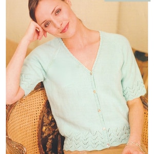 Peut inclure: Une femme porte un cardigan bleu clair à manches courtes, col en V et fermeture boutonnée. Le cardigan présente un motif décoratif sur les manches et l'ourlet. Le texte de l'image indique : "4 Ply / Fingering Yarn 86 à 132 cm de tour de poitrine."
