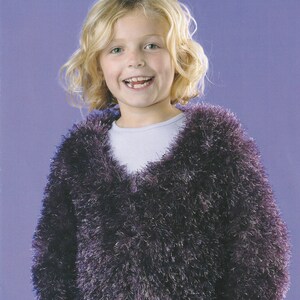 Puede incluir: Una persona joven lleva un cárdigan morado y peludo con una camisa azul claro debajo. El cárdigan mide 22-30 pulgadas de largo y 56-76 cm de ancho. El texto "COSMIC Fun Fashion knitting" está en la parte superior de la imagen.