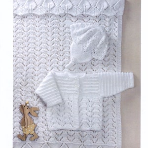 Puede incluir: Un conjunto de bebé de punto blanco que incluye un cárdigan, un gorro y una manta. El conjunto está hecho con un delicado patrón de encaje y presenta un diseño simple y clásico. 30 - 46cm, 12 - 18ins, DK.