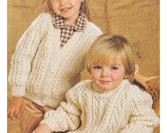 May include: Two children wearing cream colored knitted sweaters with cable knit patterns. The girl is wearing a cardigan with buttons and the boy is wearing a sweater with a turtleneck. Aran / Worsted 20 to 30 ins Sweater & Cardigan.