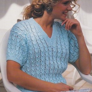 May include: A light blue knitted sweater with a v-neck and short sleeves. The sweater has a lacy pattern and is made with DK yarn.