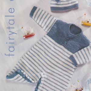 May include: A blue and white striped knitted baby onesie with a matching hat. The onesie has a blue knitted panel across the chest and the hat has a white tassel. The onesie is laid out on a white surface with a blue and white checked ribbon.
