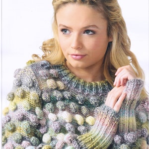 Puede incluir: Un suéter de lana gruesa con un patrón de punto de relieve en tonos de verde, azul, rosa y blanco. El suéter está disponible en tallas 81-107 cm.