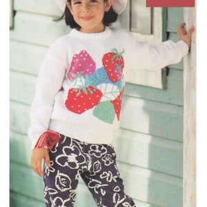 Pode incluir: Um suéter branco de malha com um desenho de morango. O suéter é usado por uma criança que usa um chapéu branco com uma faixa vermelha e calças com padrão preto e branco. O texto na imagem diz "DK / 8 Ply To Fit 1 - 14 years 20 to 34 ins".