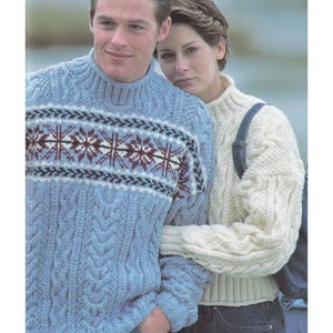 May include: A light blue cable-knit sweater with a snowflake design across the chest. The sweater is worn by a person, and the image includes text indicating sizes from 30 to 44 inches. A cream-colored cable-knit sweater is also visible.