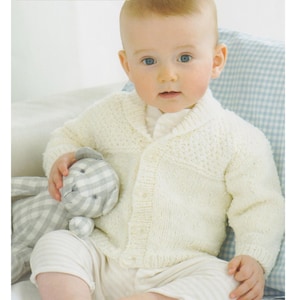 May include: A baby wearing a cream-colored knitted cardigan and striped pants, holding a gray and white stuffed animal. The image includes text that reads "DK / 8 Ply" and "0-6 months to 6-7 years 16 to 26 ins."