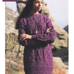 May include: Purple knitted sweater with a cable knit pattern and bobbles. The sweater is 30 to 40 inches long.  The model is wearing a purple beret and a gold necklace with a multi-colored stone pendant.  The text "DK / 8 Ply 30 to 40 ins" is in the top left corner of the image.  The text "DOUBLE KNITTING" is at the bottom of the image.