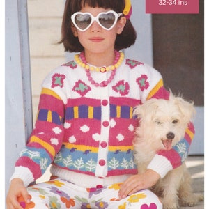 May include: A young girl wearing a white, pink, and blue striped cardigan with a heart pattern. She is wearing white pants with a floral print and heart-shaped sunglasses. She is sitting on a wooden step with a white dog beside her. The text on the image reads "DK / 8 Ply 1 to 14 years 20-22 to 32-34 ins".
