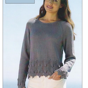 Op de afbeelding: Een grijze gebreide trui met lange mouwen en een decoratieve zoom en manchetten. De trui heeft een ronde hals en wordt gedragen met een witte broek. De tekst "Cotton DK / 8 Ply" en "32/34 to 52/54 inches" staat linksboven (ongeveer 81-137 cm).