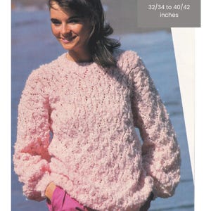 May include: A light pink textured sweater with long sleeves. The sweater is shown on a person. The image includes text that says "Sirdar Pom Pom", "3 sizes", and "32/34 to 40/42 inches".