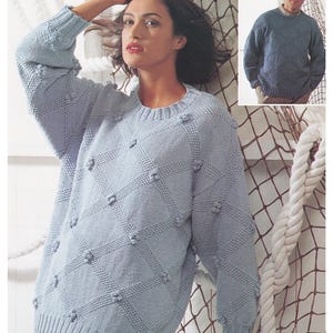 May include: A light blue knitted jumper with a diamond pattern and textured bobbles. The jumper is shown on a model and is available in sizes 32/34 to 44/46 inches.