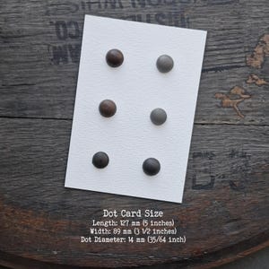 Puede incluir: Una tarjeta rectangular blanca con seis puntos circulares dispuestos en dos columnas verticales. Los puntos son de tonos marr&oacute;n, gris y negro. La tarjeta mide 127 mm de largo y 89 mm de ancho, con puntos de 14 mm de di&aacute;metro.